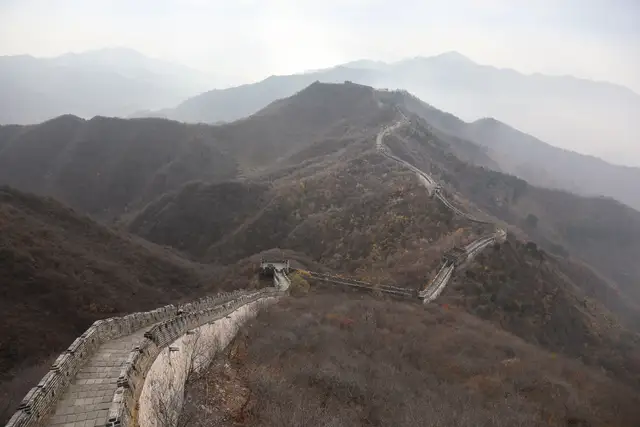 The Great Wall at Mutianyu winds over hazy autumn hills, seen from above with no visitors on the path.