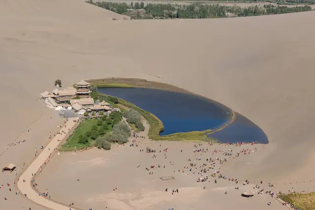 Crescent Lake in Dunhuang seen from the Mingsha dunes, a blue crescent of water beside a pagoda pavilion in the desert