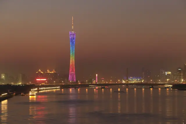 Canton Tower glowing in rainbow colours above the Pearl River in Guangzhou at dusk, with a bridge and the city skyline along the horizon.