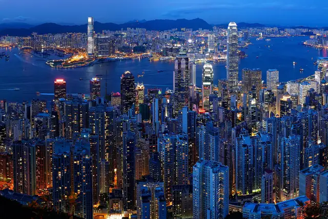 Hong Kong's skyline and Victoria Harbour at blue hour, seen from Victoria Peak, with Kowloon and its hills across the water.