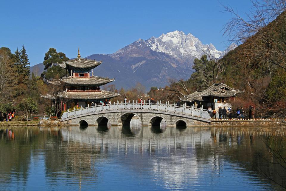 Jade Dragon Snow Mountain rising behind the pavilion and white marble bridge of Black Dragon Pool in Lijiang, reflected in the water.
