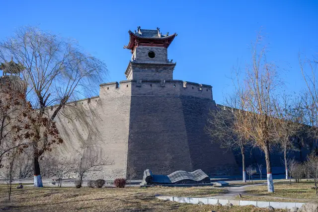 A watchtower crowns a massive corner bastion of the Ming-era city wall of Pingyao under a clear blue winter sky.