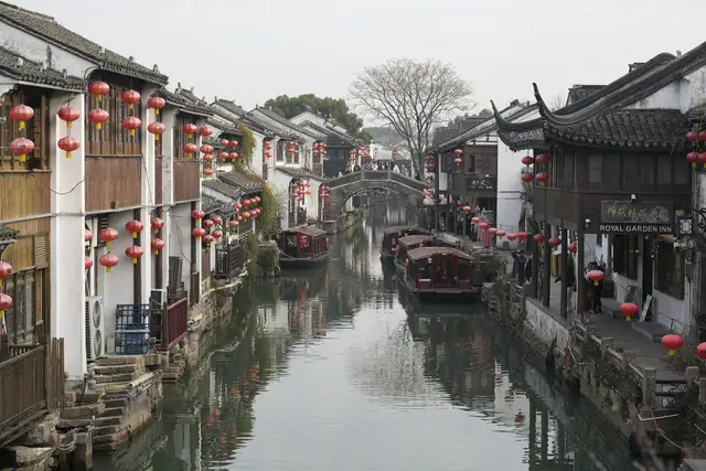 The Shantang Street canal in Suzhou under an overcast sky, lined with whitewashed houses hung with red lanterns, moored wooden boats and a stone arch bridge.