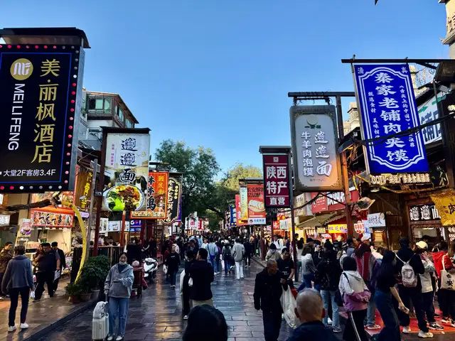 Beiyuanmen street in Xi'an's Muslim Quarter, lined with restaurant signs and busy with pedestrians in late afternoon.