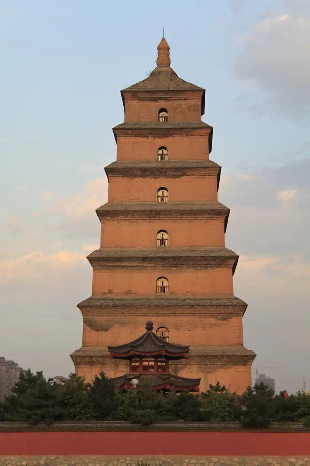 The seven-storey brick Giant Wild Goose Pagoda in Xi'an in warm evening light, above a red wall and pine trees.