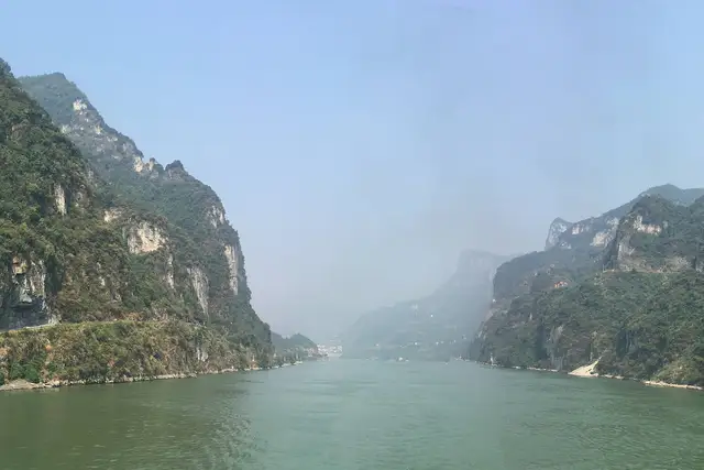 Green cliffs of Xiling Gorge rising on both banks of the Yangtze River near Yichang, the river fading into soft haze